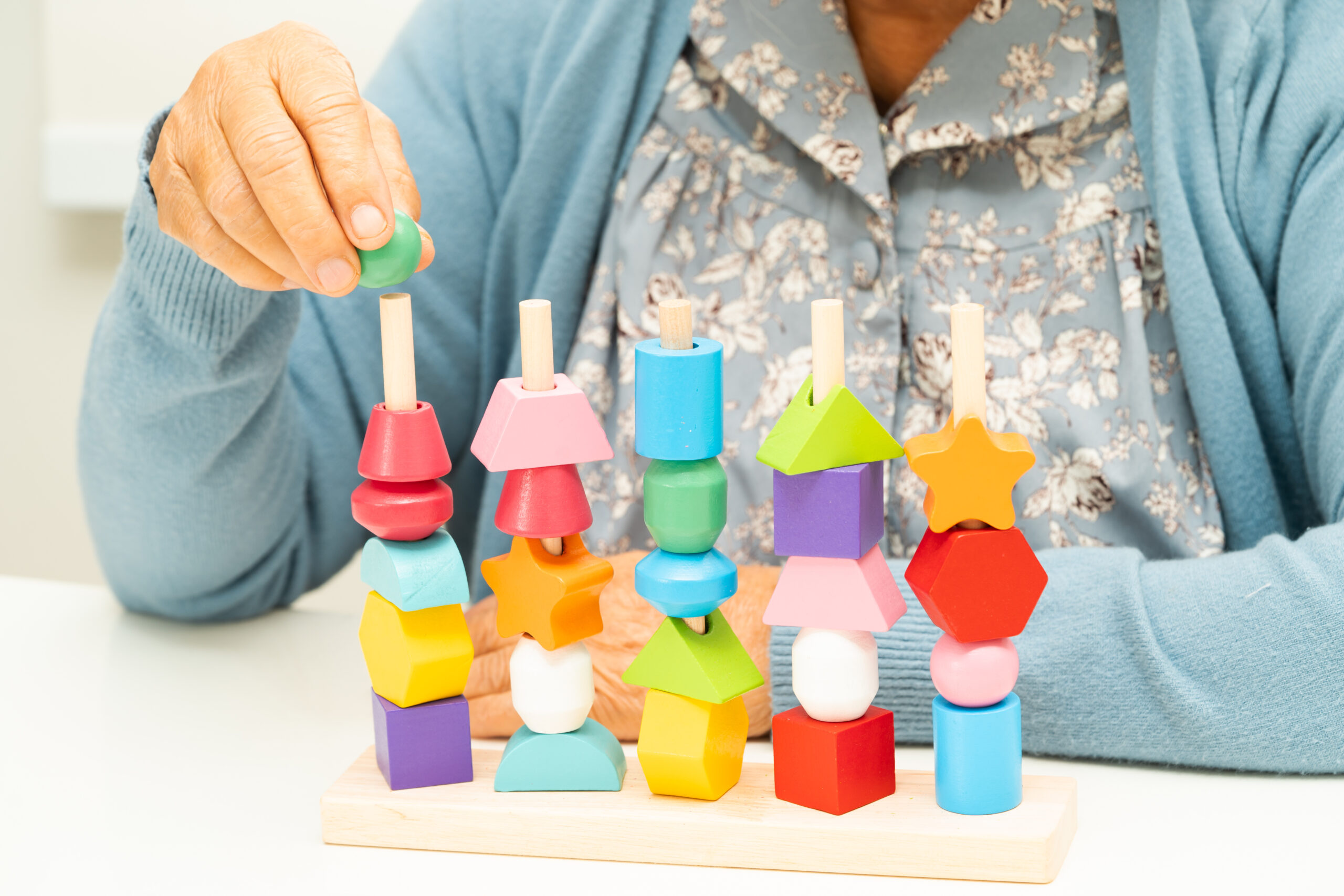 Close-up of an elderly woman’s hands as she participates in a cognitive activity using colorful wooden blocks in a memory care program.