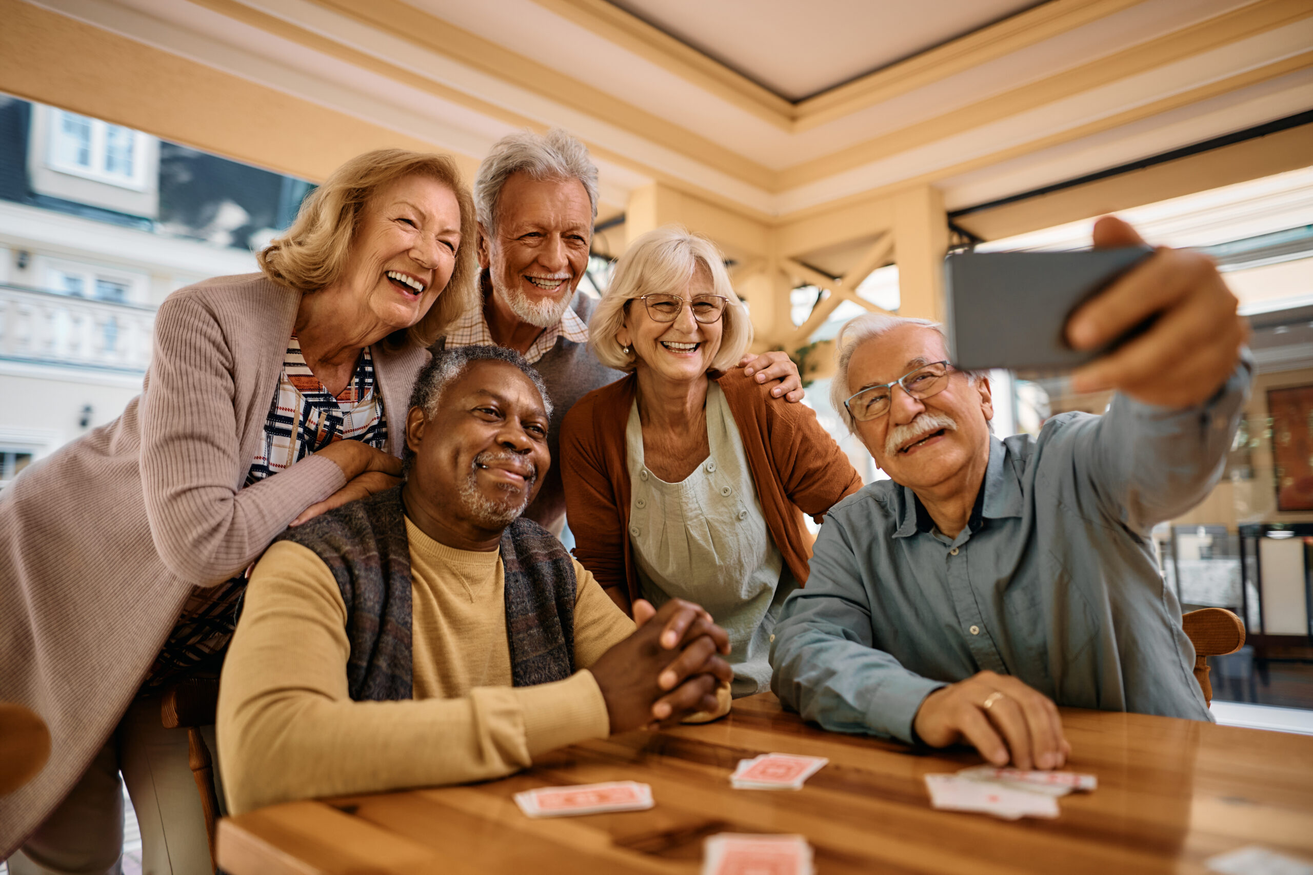 A group of smiling seniors taking a selfie together while playing cards at a senior living community in Waterford, Wisconsin.